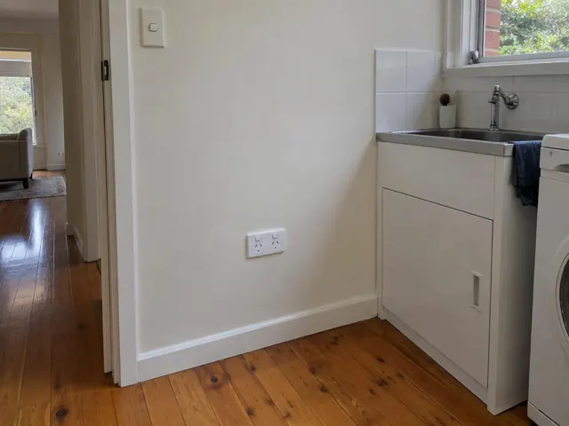 White double power point on a painted wall beside a kitchen sink and laundry area in Manly Vale