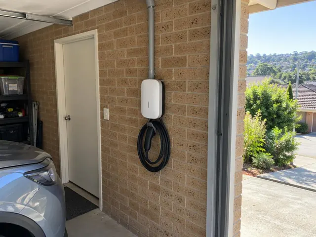 Wall-mounted EV charger on a brick garage wall beside a white door and parked car in Allambie Heights