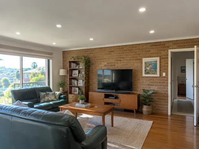 Living room ceiling with recessed downlights above a brick feature wall and timber furniture in Seaforth